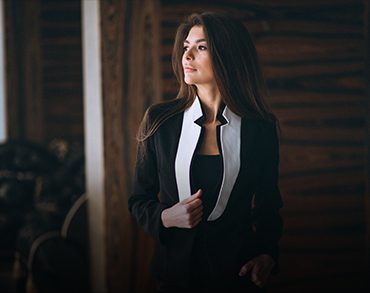 A woman in black and white suit standing next to a wooden wall.