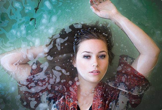 A woman is laying in the water with her arms up.