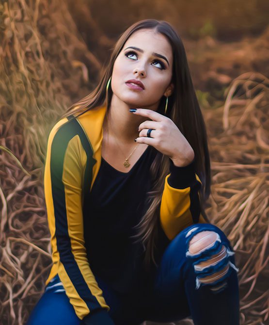 A woman sitting in the grass wearing a yellow and blue jacket.