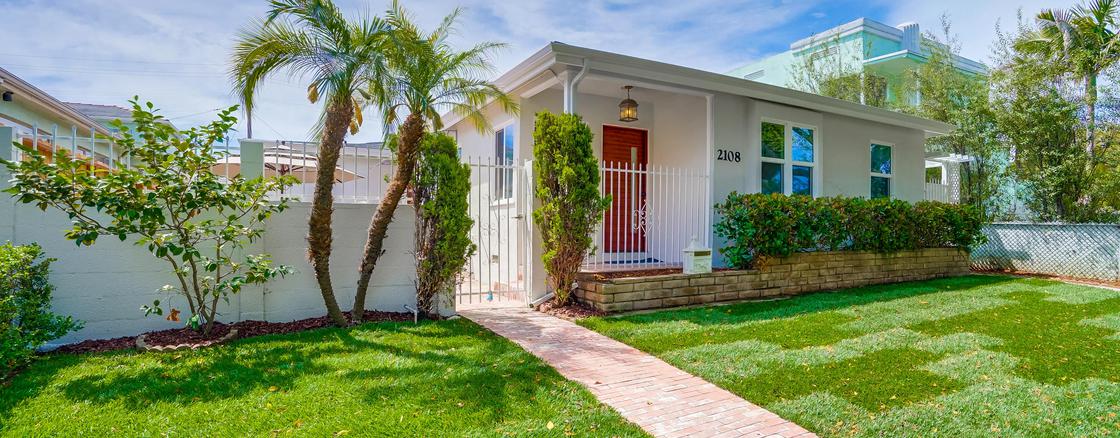 A white house with red door and palm trees.