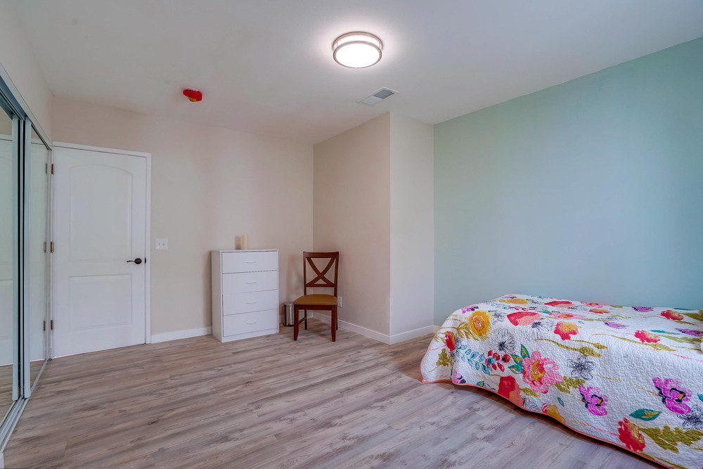 A bedroom with a bed, dresser and chair.