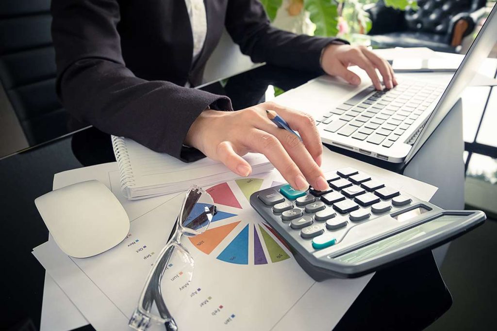 Person using calculator and laptop at desk.
