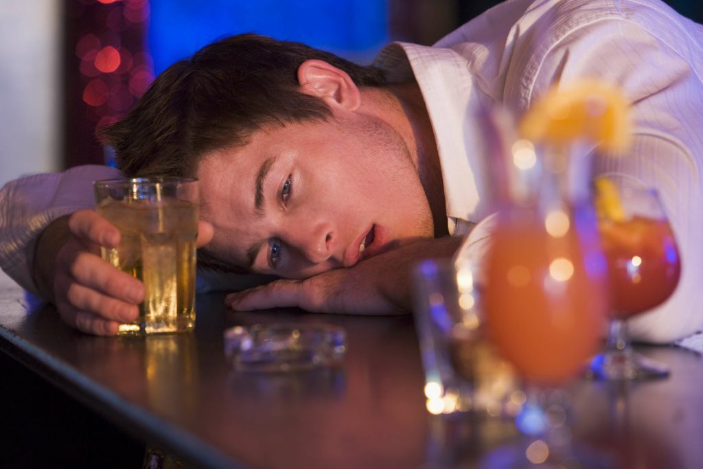 Man resting on bar with drinks nearby.